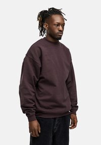 Brown sweatshirt with a high neckline, drop shoulders, and ribbed cuffs, paired with dark denim pants. Simple, solid design without patterns.