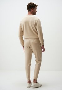 Beige sweatshirt and tapered pants in soft fabric, featuring a back pocket and cuffed hems, paired with white sneakers.