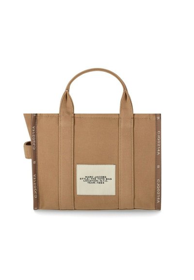 Beige canvas-kassi, jossa on kaksinkertaiset kahvat, sivussa kynäsilmukka ja valkoinen etiketti, jossa lukee "Marc Jacobs Tyylit: Kassi Sijainti: N.Y.C. Vuosi: 1984".