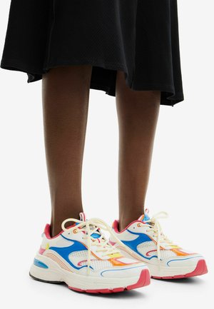 Zapatillas deportivas blancas con detalles en azul y naranja, suelas acolchadas, paneles de malla y cordones blancos. Presentan un talón rosa y un diseño de puntera redondeada.