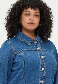 Zila džinsa jakas ar apkakli, priekšējiem pogām un sānu šuvēm. Raksturīga nedaudz brīva piegriezuma ar smalkām faktūras un stitch detaļām.