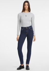 Top gris de manga larga con un pequeño logo de estrella negra, combinado con unos jeans ajustados de cintura alta en azul oscuro con bolsillos frontales y costuras en contraste.