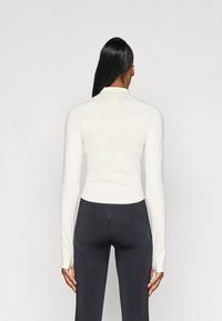 Lettet, tætsiddende langærmet top i creme med høj hals og raglanærmer, parret med mørke strømpebukser med strukturerede accenter.