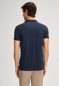 Marineblauw polo shirt met korte mouwen, een klassieke kraag, een zachte textuur en een subtiele logo-detail aan de zoom, gecombineerd met beige broek.