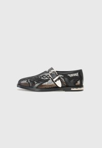 Black mesh shoe with a rounded toe, decorative buckle, and intricate lace pattern on the upper. Flat sole with a subtle scalloped edge.