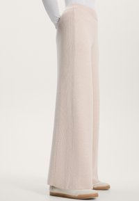 Ljusrosa vida byxor tillverkade av ribbat material med en slät textur, med hög midja och kontrasterande sidopaneler.