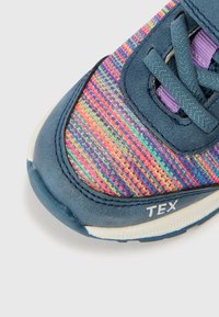 Baskets bleues avec une tige en tissu texturé aux rayures multicolores, un col rembourré, des accents violets et une semelle blanche avec détail du logo.