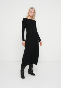 Black ribbed knit dress with long sleeves, off-the-shoulder neckline, and side slit. Paired with black ankle boots and smooth texture.