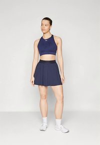Tengerészkék sportos crop top logóval, hozzáillő, szűkülő szoknyával párosítva. Az anyag sima; az egész kialakítás testhezálló és atletikus.