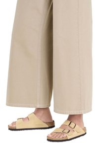 Infradito Birkenstock con tomaia in morbida suede beige, due cinturini regolabili con fibbie in metallo e plantare sagomato in sughero.