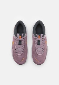 Violet verkkokangasjuoksukengät harmailla yksityiskohdilla, joissa on mustat nauhat, oranssi logo ja teksturoitu pinta valkoisella pohjalla.