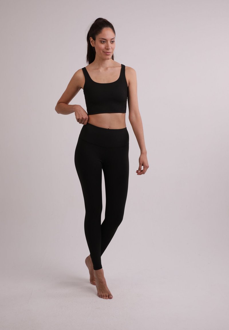 Černý sportovní crop top a odpovídající legíny, oboje vyrobené z hladkého, pružného materiálu. Střih je přiléhavý s vysokým pasem.