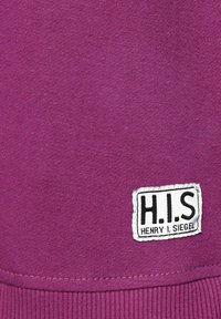Tela de algodón morada con una textura suave, que presenta una etiqueta blanca con texto negro que dice "H.I.S" y "HENRY I. SIEGEL" cosido en ella.