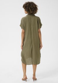 Rochie de culoare verde oliv, ușoară, cu o croială lejeră, mâneci scurte și o textură pliată. Fantele laterale și tivul drept îmbunătățesc libertatea de mișcare.