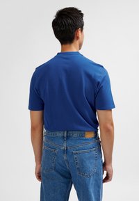 Niebieska koszulka z krótkim rękawem i okrągłym dekoltem, zestawiona z jasnoniebieskimi, wysokim stanem jeansami z naszywką ze skóry z tyłu.