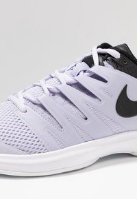 Fialová sportovní obuv s horní částí z síťoviny a syntetického materiálu, s černými akcenty a černým logem, a bílou mezipodešví. Viditelný systém šněrování.