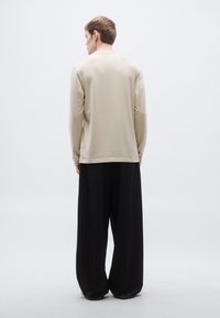 Hosszú ujjú, bézs felső egyszerű dizájnnal, laza fekete nadrággal párosítva. Sima anyagtextúra, laza szabás és minimális részletezés.