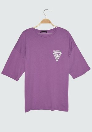 Lila übergroßes T-Shirt mit weißem geometrischem "CALIFORNIA LA"-Logo auf der linken Brust, an einem Holzkleiderbügel vor weißem Hintergrund hängend.
