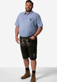 Camisa de cuadros azul claro de manga corta con emblema de ciervo, pantalones cortos de ante negros con bordado dorado, botas de cordones marrones y calcetines azules.