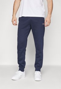 Marineblaue Sweatpants aus weichem Material, mit einem elastischen Bund und Bündchen, einem kleinen Logo am linken Oberschenkel und einem lässigen Schnitt.