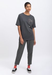 Grijze oversized t-shirt met een kleurrijk abstract ontwerp, gecombineerd met donkergrijze broek en zwarte sneakers, met oranje en grijze gestreepte sokken.