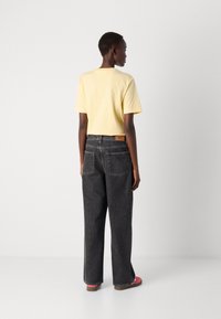Gul crop topp med høyt liv sorte jeans. Jeansene har et strukturert stoff og to baklommer, med rosa fottøy.