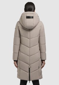 Gepolsterter langer Mantel in hellbeige mit Zickzackmuster, Kapuze und einem Reißverschluss vorn. Verfügt über ein Logo-Patch auf der Rückseite.