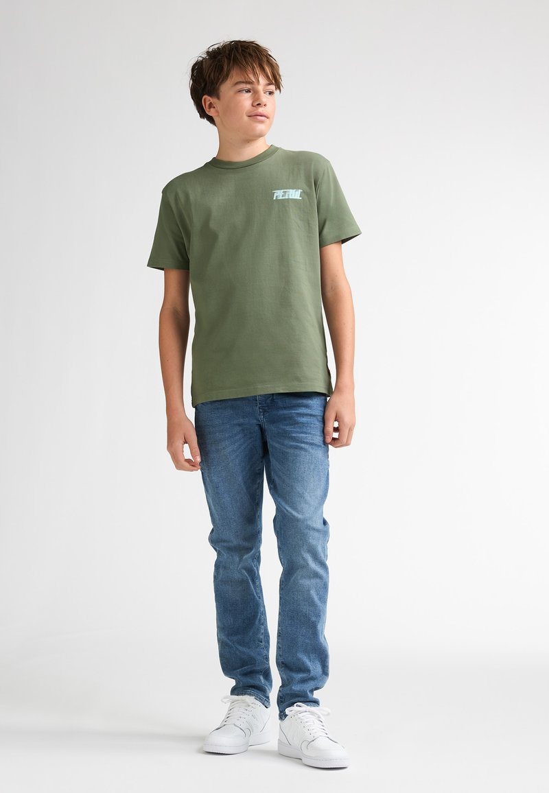 Grøn bomuld T-shirt med korte ærmer og en lille grafik på brystet, parret med lyseblå denimjeans og hvide sneakers.