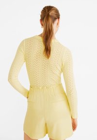 Top giallo a maniche lunghe con un motivo zigzag testurizzato, abbinato a pantaloni corti giallo chiaro. I pantaloni corti presentano una vita elastica e tasche posteriori.