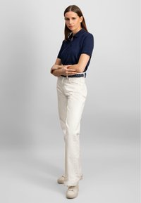 Marineblå polo skjorte, kremfargede rette bukser, flettet mørk belte, og beige joggesko. Glatte teksturer, enkel design, tettsittende kutt.