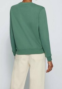 Grön sweatshirt med långa ärmar, ribbade muddar och fåll, tillverkad av mjukt tyg. I kombination med ljusbeigavida byxor.