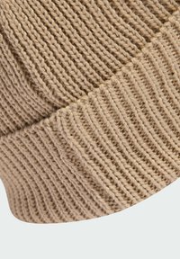 Bežová pletená čiapka s ribovanou textúrou. Má prehnutý okraj a mäkkú, hustú priadzu pre teplo.
