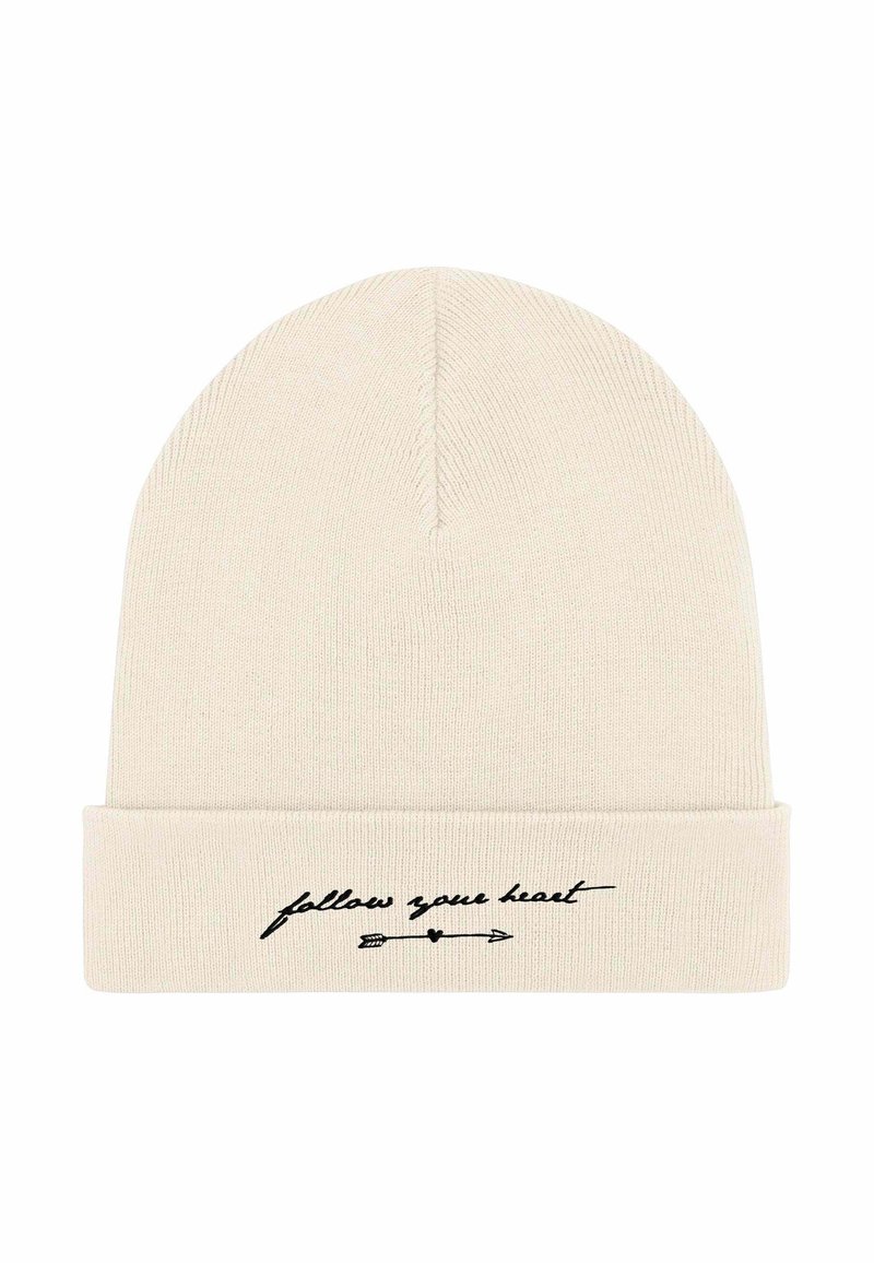 Cappellino a maglia in beige chiaro con risvolto. Presenta un testo corsivo nero "segui il tuo cuore" e una grafica con una freccia. Tessuto morbido.