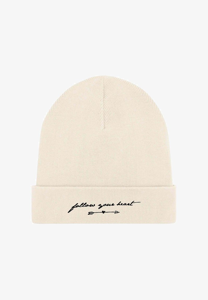 Cappellino a maglia in beige chiaro con risvolto. Presenta un testo corsivo nero "segui il tuo cuore" e una grafica con una freccia. Tessuto morbido.