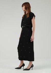 Vestido negro con un cuerpo ajustado y una falda fluida, adornado con embellishments de flores negras y un cinturón en la cintura. Textura de tela suave.
