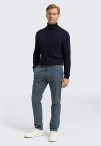 Marinefarbener Rollkragenpullover, Slim Fit, gerippte Textur; graue maßgeschneiderte Hosen, schmale Beine; weiße Sneakers mit strukturierten Akzenten.