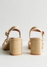 Beige strappy heels with a woven texture, a thick block heel, and an adjustable ankle strap, designed for comfort and support.
