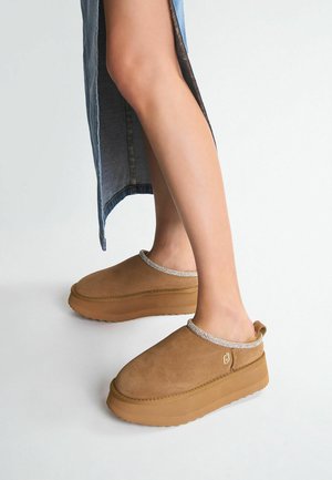 Clog in suede marrone con suole in gomma spesse e colli testurizzati con accenti metallici; punte arrotondate e design slip-on. Suola testurizzata per una migliore aderenza.