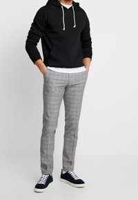 Czarna bluza z kapturem z kieszenią kangurką, szare spodnie w kratę, oraz granatowe sneakersy z białymi podeszwami i sznurowadłami. Casualowy i monochromatyczny strój.
