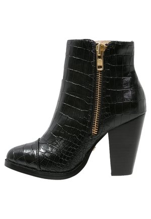 Bottine noire en cuir à texture crocodile avec fermeture éclair dorée et talon haut carré empilé.