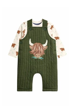 Groene gevoerde overall met een geborduurde koeienkop, gecombineerd met een shirt met lange mouwen bedrukt met kleine bruine koeien op een witte achtergrond.