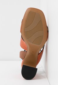 Sandale à talon haut orange avec motif texturé, semelle en caoutchouc et talon bloc noir, taille 37, photographiée du côté de la semelle.