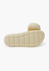 Sole della scarpa di colore crema con superficie testurizzata e motivo di battistrada prominente; sezione del tacco arrotondata con leggere indentazioni e dettaglio di branding.