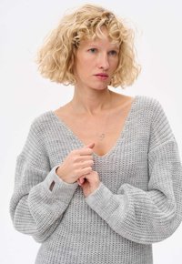 Szary dziany sweter z szerokim dekoltem w kształcie litery V, oversize'owymi rękawami i prążkowanymi mankietami. Tkanina ma teksturowany wzór z subtelnymi wariacjami.