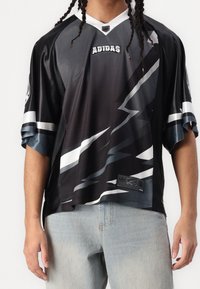 Mustan ja harmaan värinen adidas-paita, jossa on verkkotekstuuri, lyhyet hihat, V-pääntie, valkoisilla viivoilla ja rinnassa logolla varustettuna.