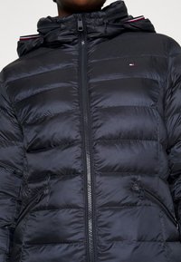 Svart puffjacka med quiltat mönster, utrustad med blixtlås och sidofickor. Med huva och kontrasterande randiga detaljer.