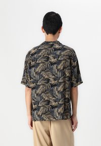 Camisa de manga corta con un fondo negro y un patrón de hojas de palma doradas. Tela suave con un ajuste relajado y diseño de cuello.