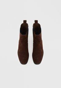 Barna szarvasbőr bokacsizma, sima textúrával, rugalmas oldalpanelekkel és lehúzófülekkel a könnyű felvételért. Kerek orrú és tartós gumitalpú.