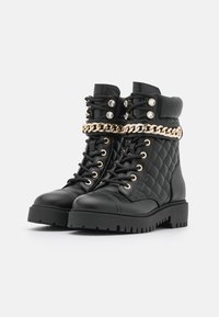 Czarne pikowane skórzane botki sięgające kostki z detalami w postaci złotego łańcucha i oczkami, z grubą żebrowaną podeszwą i sznurowanym zapięciem.