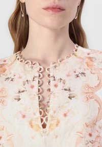 Top de tela ligera con patrón floral y escote en forma de ondas. Colores pasteles suaves: melocotón, rosa y crema, que crean un diseño delicado.